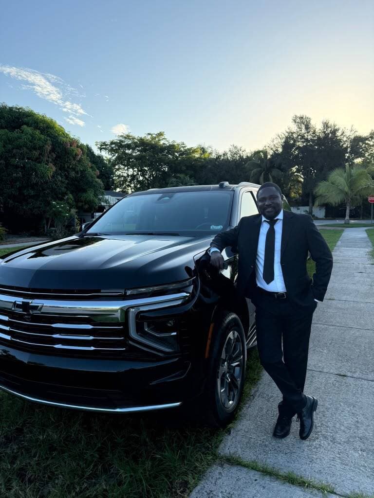 Worldtrans Services chauffeur in a suit standing beside a black Chevrolet Suburban
